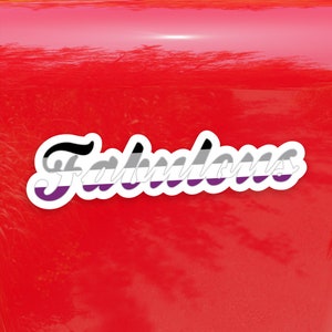 May include: A black, white, and purple sticker with the word "Fabulous" in a stylized font. The sticker is on a red surface.