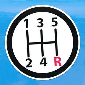 Può includere: Un cerchio bianco con bordo nero raffigurante uno schema del cambio. I numeri 1, 3 e 5 sono in alto, 2 e 4 in basso, e la lettera R è rossa. Lo sfondo è azzurro.