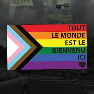 May include: A rainbow pride flag with a black triangle in the top left corner. The flag has the text "TOUT LE MONDE EST LE BIENVENU ICI" in black text with a black heart at the bottom.