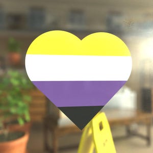 May include: A heart-shaped sticker with the colors of the non-binary pride flag. The flag is yellow, white, purple, and black.