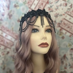 May include: A black beaded headband with a fringe of black beads. The headband is worn by a person with long, wavy, light purple hair.