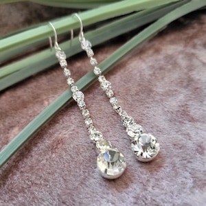 Peut inclure: Une paire de longues boucles d'oreilles pendantes en argent avec des pierres de cristal claires. Les boucles d'oreilles ont un cristal en forme de larme au bas.