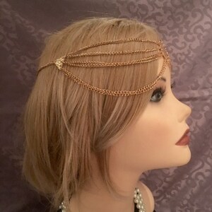 May include: Gold chain headpiece with multiple strands of chain and a small, sparkly, triangular accent.