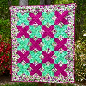 May include: A quilt with a patchwork design featuring alternating squares of pink and teal fabric. The fabric has a floral pattern.