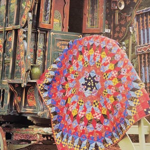 May include: A book cover titled Kaffe Fassett's Caravan of Quilts featuring a colorful patchwork quilt with red, yellow, blue, and black geometric star patterns draped over a dark green, ornately painted wooden caravan with floral details.