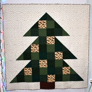 May include: A patchwork quilt featuring a green and brown Christmas tree design. The tree is made up of squares of different fabrics, including plaid and a pattern of fish.
