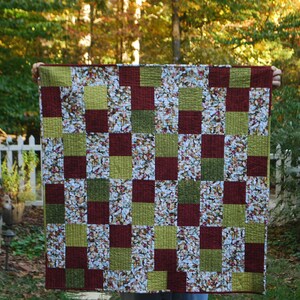 May include: A quilt with a checkered pattern in shades of green, brown, and white. The quilt is made of fabric with a floral print.