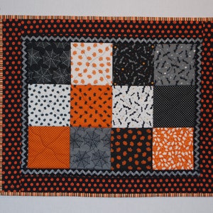May include: A black and orange Halloween quilt with a patchwork design featuring bats, pumpkins, and spiderwebs. The quilt has a black and orange polka dot border.