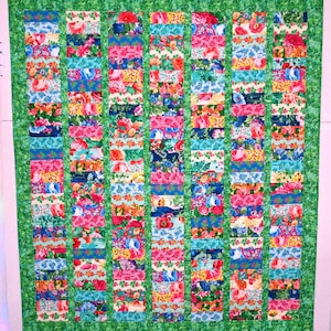 May include: A colorful handmade quilt with a floral pattern. The quilt features vertical columns of rectangular patches in various floral prints, including pink, blue, and yellow. The quilt is bordered with a green floral fabric.