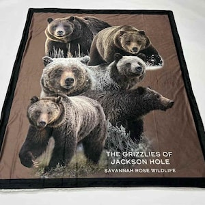May include: A brown and black blanket featuring a group of grizzly bears. The blanket has a black border and the text "THE GRIZZLIES OF JACKSON HOLE SAVANNAH ROSE WILDLIFE".