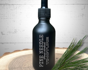 May include: A black tincture bottle with a dropper, labeled "PINE NEEDLE (Pinus strobus) TINCTURE" in white text. A sprig of green pine needles rests on a wooden surface next to the bottle. The background is a white, weathered wood.