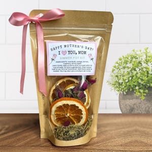 May include: A clear cellophane bag tied with a pink ribbon, containing a simmer pot kit. The kit includes dried orange slices, rose buds, and herbs. A label reads "Happy Mother's Day! I Love You, Mom".