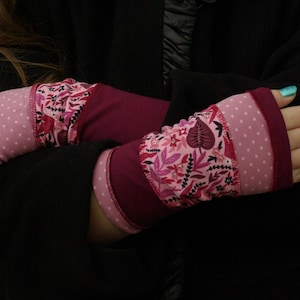 Op de afbeelding: Een paar roze en bordeauxrode vingerloze handschoenen met een bloemenpatroon. De handschoenen hebben een stippenpatroon op de pols.