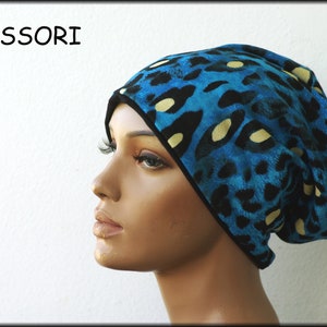 Könnte beinhalten: Eine blaue Mütze mit einem schwarzen und gelben Leopardenmuster. Die Mütze wird von einer Schaufensterpuppe getragen. Das Wort "ACCESSORI" ist oben links im Bild in Schwarz gedruckt.