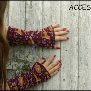 May include: Burgundy arm warmers with a fox and floral pattern. The text "ACCESSORI" is visible in the upper right corner. The background is a weathered, white wooden surface.