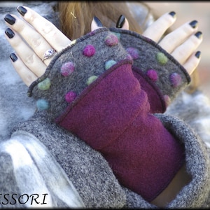 Könnte beinhalten: Ein Paar graue und violette fingerlose Handschuhe mit bunten Filzpunkten. Die Handschuhe haben einen umschlagbaren Bund.