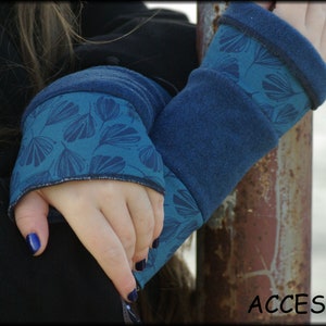 Könnte beinhalten: Ein Paar blaue Fleece-Handwärmer mit einem teal- und weißen Blumenmuster. Die Handwärmer sind umgeklappt und die Hand der Person, die sie trägt, ist sichtbar.