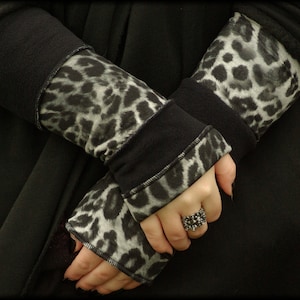 Könnte beinhalten: Ein Paar schwarze und weiße fingerlose Handschuhe mit Tiermuster und schwarzem Bündchen. Die Handschuhe sind aus weichem, dehnbarem Stoff und haben eine bequeme Passform.