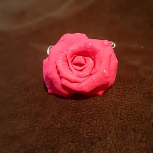 May include: A bright pink rose with a shiny, wet finish. The rose is made of a smooth, pliable material and has a realistic appearance.