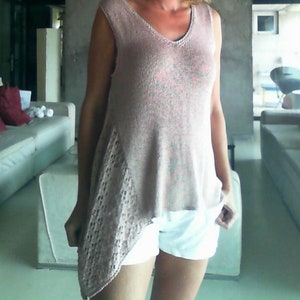 May include: A sleeveless, light pink knit top with a V-neck and an asymmetrical lace panel. The top is paired with white shorts. The woman in the image has blonde hair.