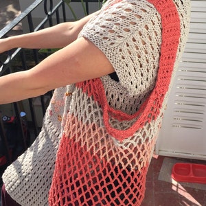 Puede incluir: Un top de crochet beige de tejido abierto con mangas cortas y un bolso de hombro color coral. El bolso es de diseño tipo red, con un degradado coral-beige. El top tiene un diseño suelto y aireado.