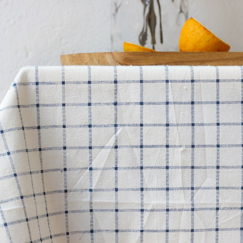 May include: A white tablecloth with a blue and white checkered pattern. The tablecloth is draped over a wooden table.