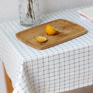 May include: A white tablecloth with a blue checkered pattern, a wooden serving tray with two lemon halves on top, and a clear glass vase with dried flowers.