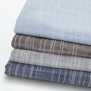 May include: Four different fabric swatches stacked on top of each other. The top swatch is light blue with a subtle white stripe pattern. The second swatch is brown with a white stripe pattern. The third swatch is grey with a white stripe pattern. The bottom swatch is dark blue with a white stripe pattern.