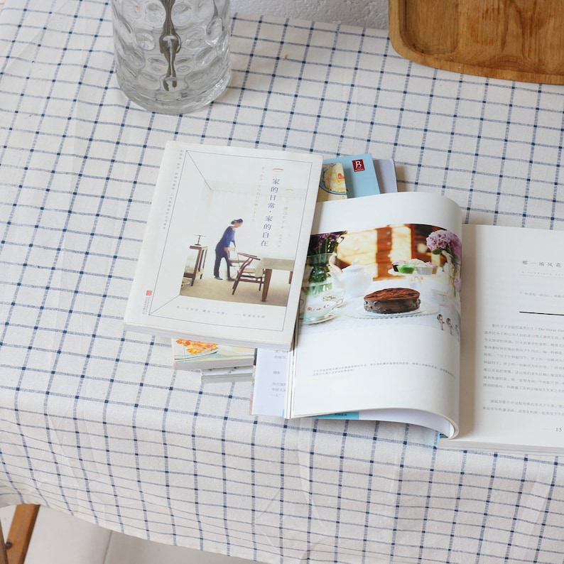 May include: A stack of books with a white checkered tablecloth. The top book has a photo of a chocolate cake on a plate with flowers and a teapot. The book title is "The Daily Rituals of the Creative Class".