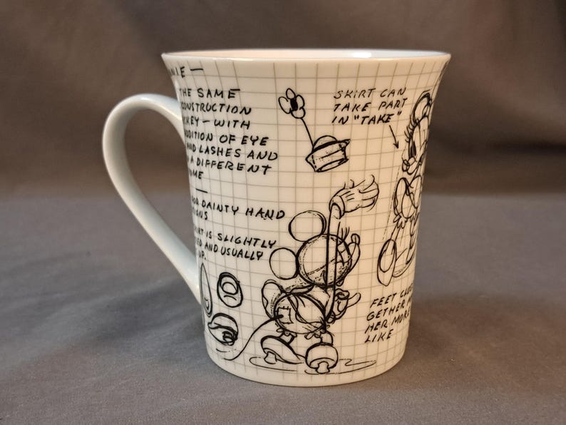 Op de afbeelding: Witte keramische mok met een zwart-witte illustratie van Mickey Mouse en Minnie Mouse. De mok heeft een handvat en bevat tekst over het ontwerp van de personages.
