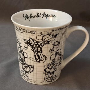 Op de afbeelding: Witte keramische koffiemok met een zwart-witte illustratie van Minnie Mouse. De mok heeft de tekst "Minnie Mouse" aan de voorkant.