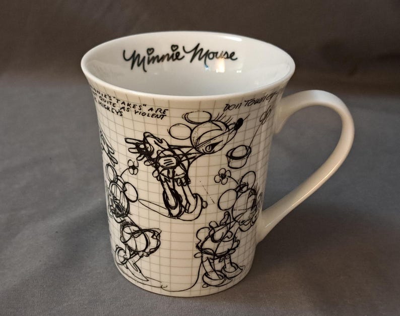 Op de afbeelding: Witte keramische koffiemok met een zwart-witte illustratie van Minnie Mouse. De mok heeft de tekst "Minnie Mouse" aan de voorkant.