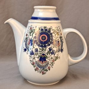 May include: White ceramic teapot with a blue and floral design. The teapot has a lid and a handle.