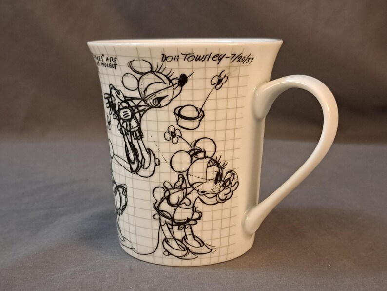 Op de afbeelding: Witte keramische mok met een zwart-witte schets van Mickey Mouse op een geruit achtergrond. De mok heeft een handvat en de tekst "Don Towley - 7/20/17" staat op de zijkant gedrukt.