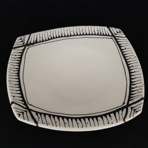 May include: A white ceramic plate with a black geometric design around the edge.