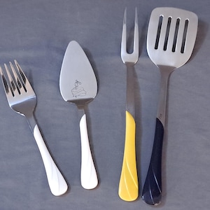 May include: Four kitchen utensils with white and yellow handles. A cake server, a fork, a fork with a yellow handle, and a spatula with a blue handle.