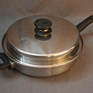 May include: A stainless steel pot with a lid and a black handle. The pot has a shiny finish and is suitable for cooking on the stovetop.