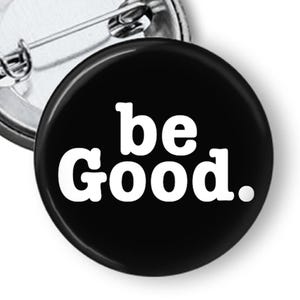 May include: Black button with the words "be Good." in white, with a pin back. The button is round and has a glossy finish. The pin is silver and attached to the back of the button.