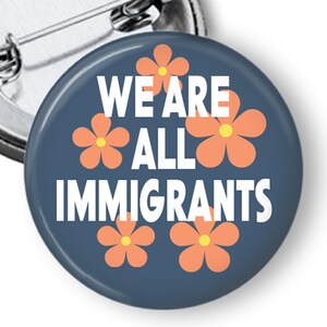 May include: A blue button with the text "We are all immigrants" in white and four orange flowers.