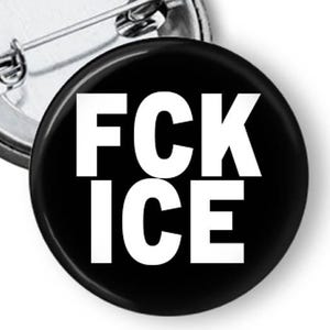 Puede incluir: Un bot&oacute;n negro con el texto blanco "FCK ICE". El bot&oacute;n es redondo y tiene un respaldo de alfiler met&aacute;lico. Otro bot&oacute;n es parcialmente visible en el fondo.