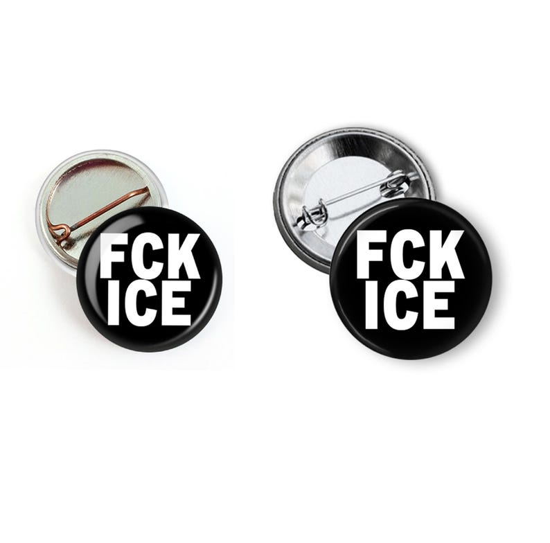 Puede incluir: Dos insignias redondas negras con el texto blanco "FCK ICE". Una insignia muestra la parte trasera del alfiler, la otra la parte delantera. Las insignias est&aacute;n sobre un fondo blanco.