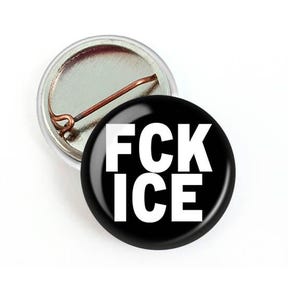 Puede incluir: Un bot&oacute;n negro con el texto blanco "FCK ICE" se muestra junto a un respaldo de bot&oacute;n. El bot&oacute;n tiene un acabado brillante y brillante. La parte posterior del bot&oacute;n es plateada con un alfiler de cobre.