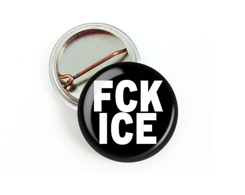 Puede incluir: Un bot&oacute;n negro con el texto blanco "FCK ICE" se muestra junto a un respaldo de bot&oacute;n. El bot&oacute;n tiene un acabado brillante y brillante. La parte posterior del bot&oacute;n es plateada con un alfiler de cobre.