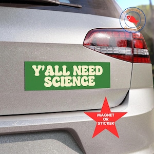 May include: A green rectangular magnet or sticker with the text "Y'ALL NEED SCIENCE" in cream-colored, retro-style lettering. A red star-shaped sticker indicates the item is available as a magnet or sticker.