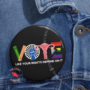 May include: A black badge featuring the word "VOTE" in various colours and symbols, including a rainbow flag, a fist, and a uterus. The text "LIKE YOUR RIGHTS DEPEND ON IT" is also included.