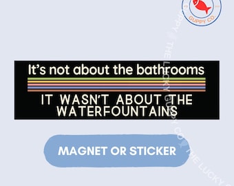May include: A rectangular black magnet or sticker featuring the white text It's not about the bathrooms and IT WASN'T ABOUT THE WATERFOUNTAINS, separated by a series of horizontal stripes in yellow, green, blue, purple, and orange colors.