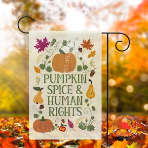May include: A garden flag with a fall theme. The flag features a large orange pumpkin, leaves, and pears, with the text "PUMPKIN SPICE & HUMAN RIGHTS". The flag is mounted on a black metal stand.