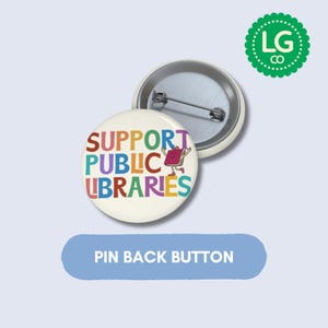 May include: A round pin back button with a cream-colored background featuring the multi-colored text SUPPORT PUBLIC LIBRARIES and a small cartoon book character. The back of the button is metallic silver with a horizontal pin mechanism attached.