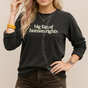 May include: Dark gray long-sleeve shirt with the text "big fan of human rights" in white. The shirt has a crew neck and long sleeves. The Lucky Guppy Co. logo is printed on the side.