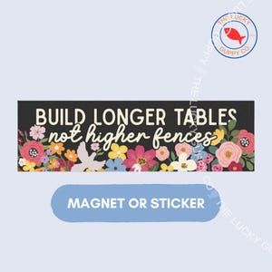 May include: A rectangular magnet or sticker featuring a black background with the white text BUILD LONGER TABLES not higher fences. The design is decorated with a colorful floral arrangement including pink, red, yellow, and blue flowers.